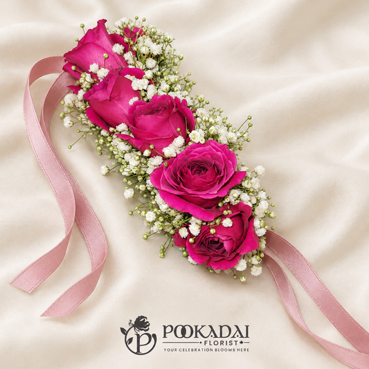 Magenta mini roses surrounded by white baby’s breath in an elongated floral accessory with pink satin ribbon ties.